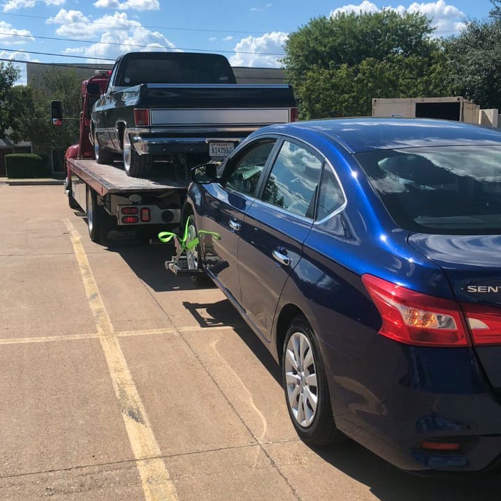 Towing pickup on a flatbed with a nissan sentra towed behind.